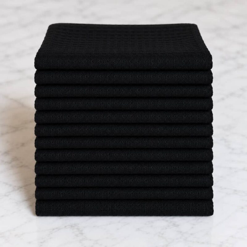 Pile de 12 torchons Gaufrex® noirs garantis grand teint en coton gaufré, sur un plan en marbre